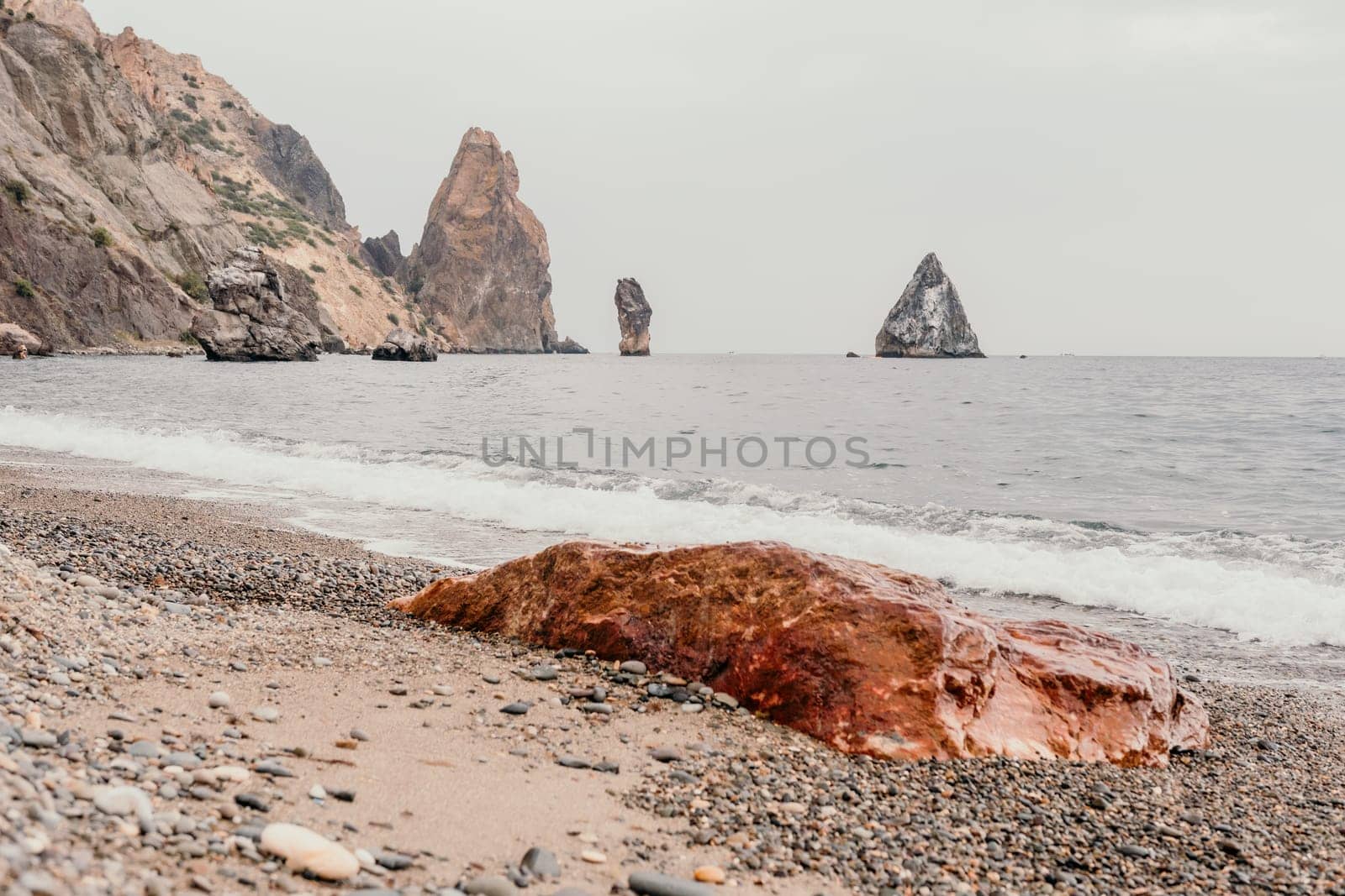 Large red jasper rock on the beach, with the sea in the background. Big Red Jasper Stone Close Up by panophotograph