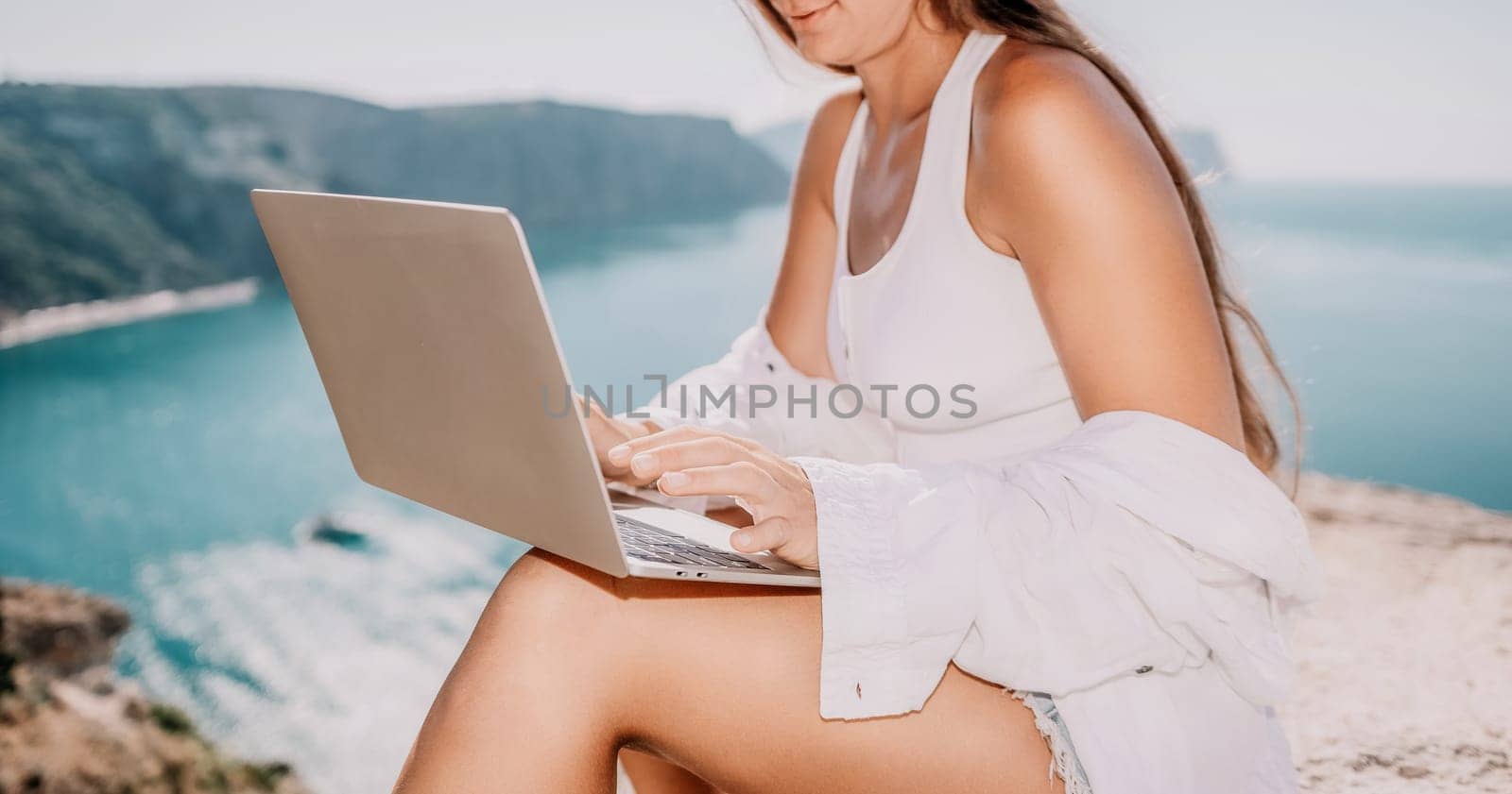 Digital nomad, Business woman working on laptop by the sea. Pretty lady typing on computer by the sea at sunset, makes a business transaction online from a distance. Freelance remote work on vacation