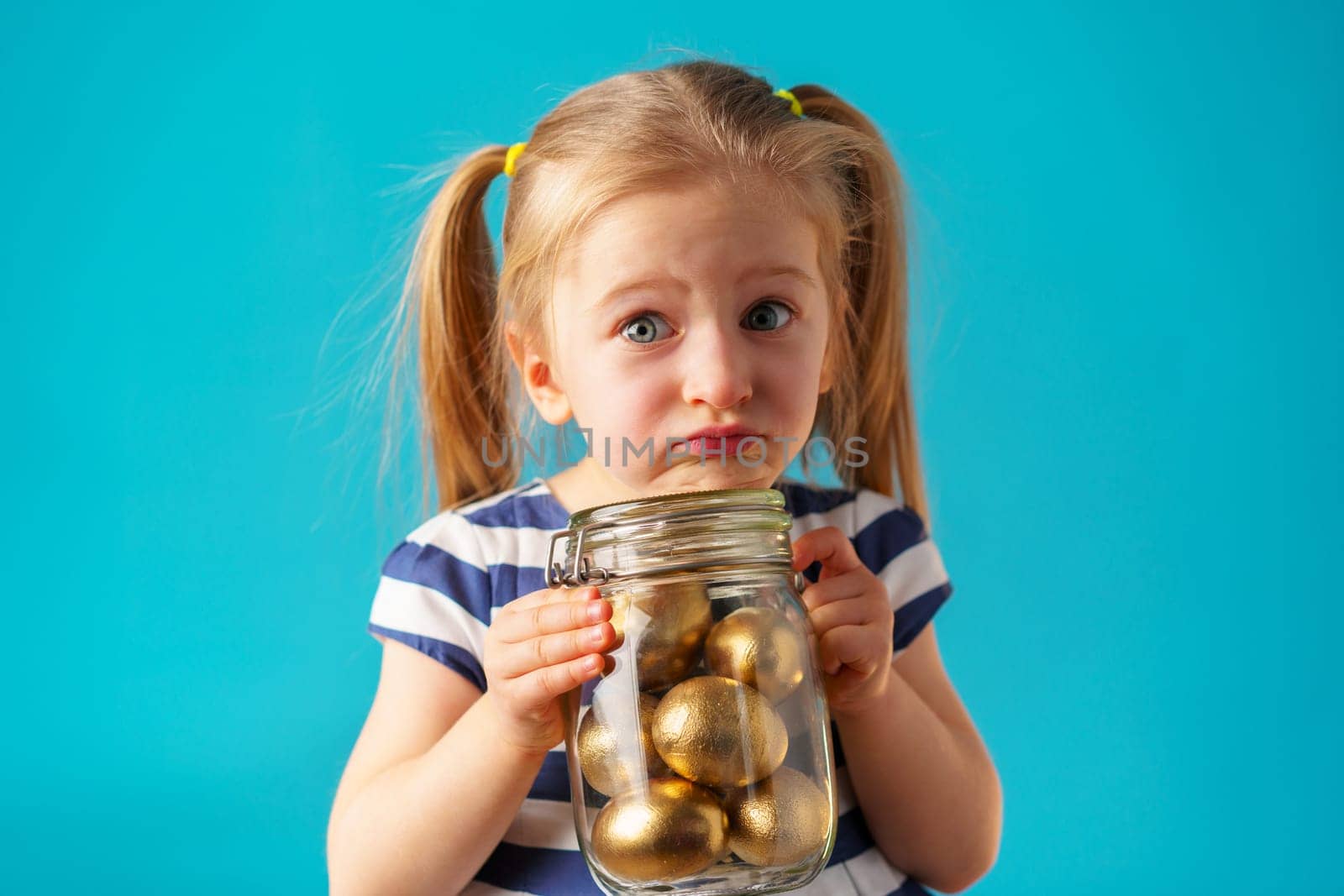 Blonde toddler girl with glass jar full of golden painted eggs for Easter