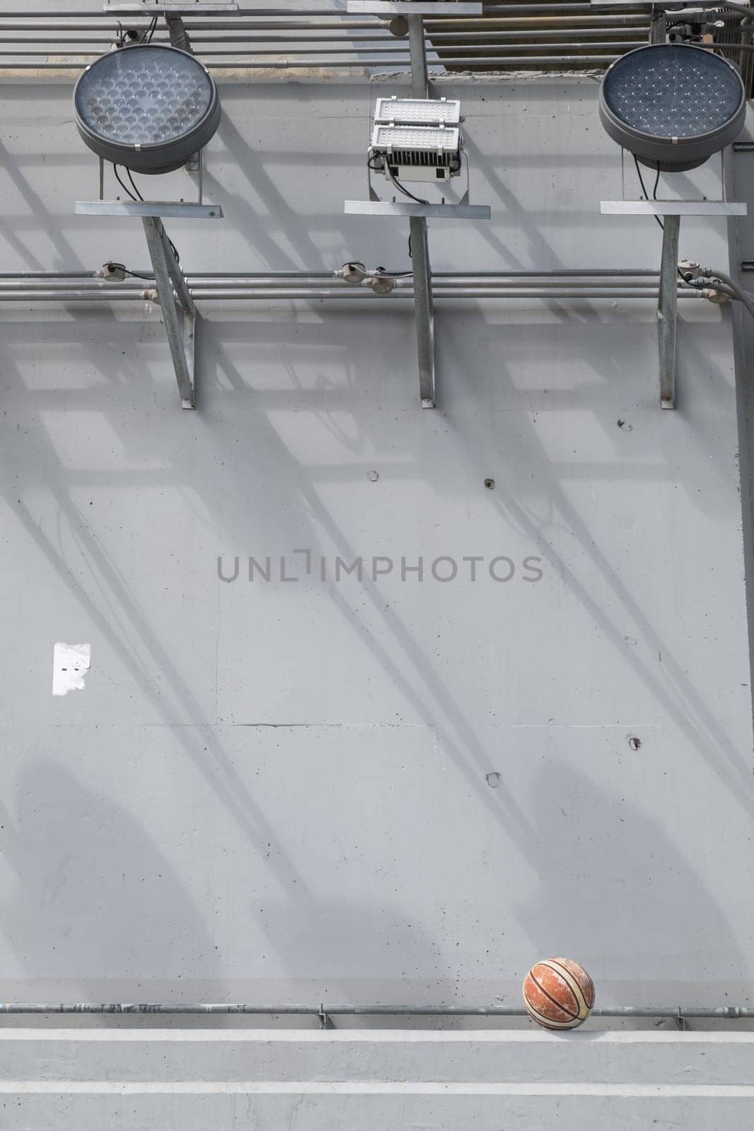 Bangkok, Thailand - 28 Sep, 2024 - Old basketball ball on cement floor under LED flood lights spotlights of Bridge foundation post. Space for text, Selective focus.