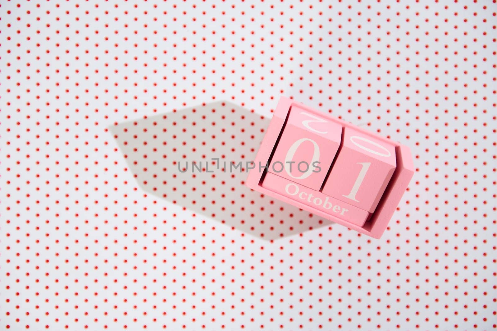 A pink block calendar displaying October 1st on a backdrop of red polka dots, casting a sharp shadow.