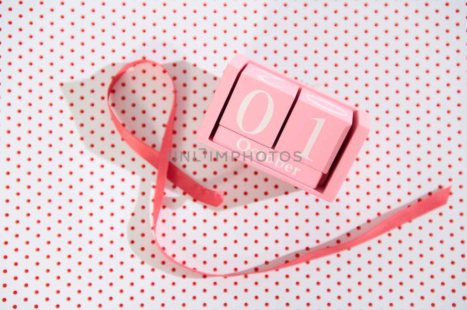 Pink cube calendar displaying October 1st, accompanied by a ribbon on a polka-dot background.