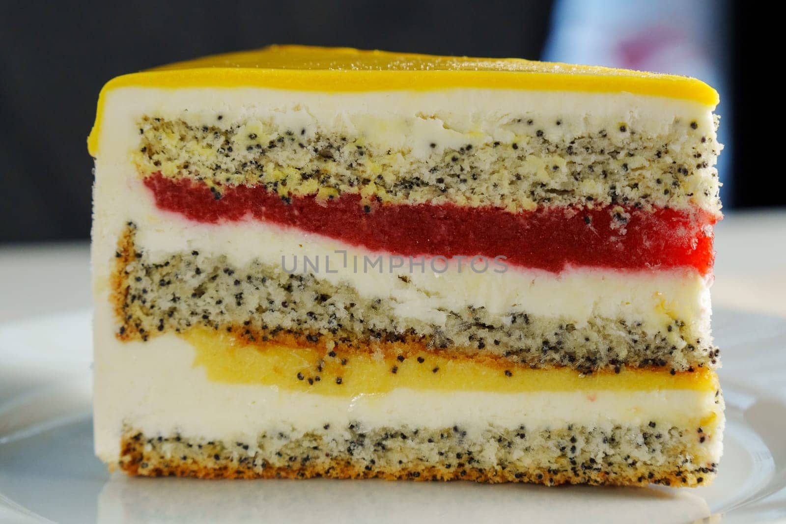 A stunning cross-section of a colorful layer cake featuring poppy seeds, cream, and vibrant fruit jelly on a sunny afternoon