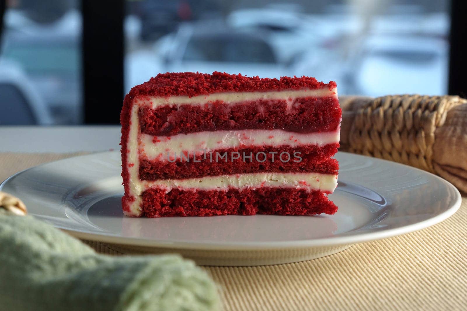 A tempting slice of red velvet cake sits on a simple white plate, showcasing layers of creamy frosting.