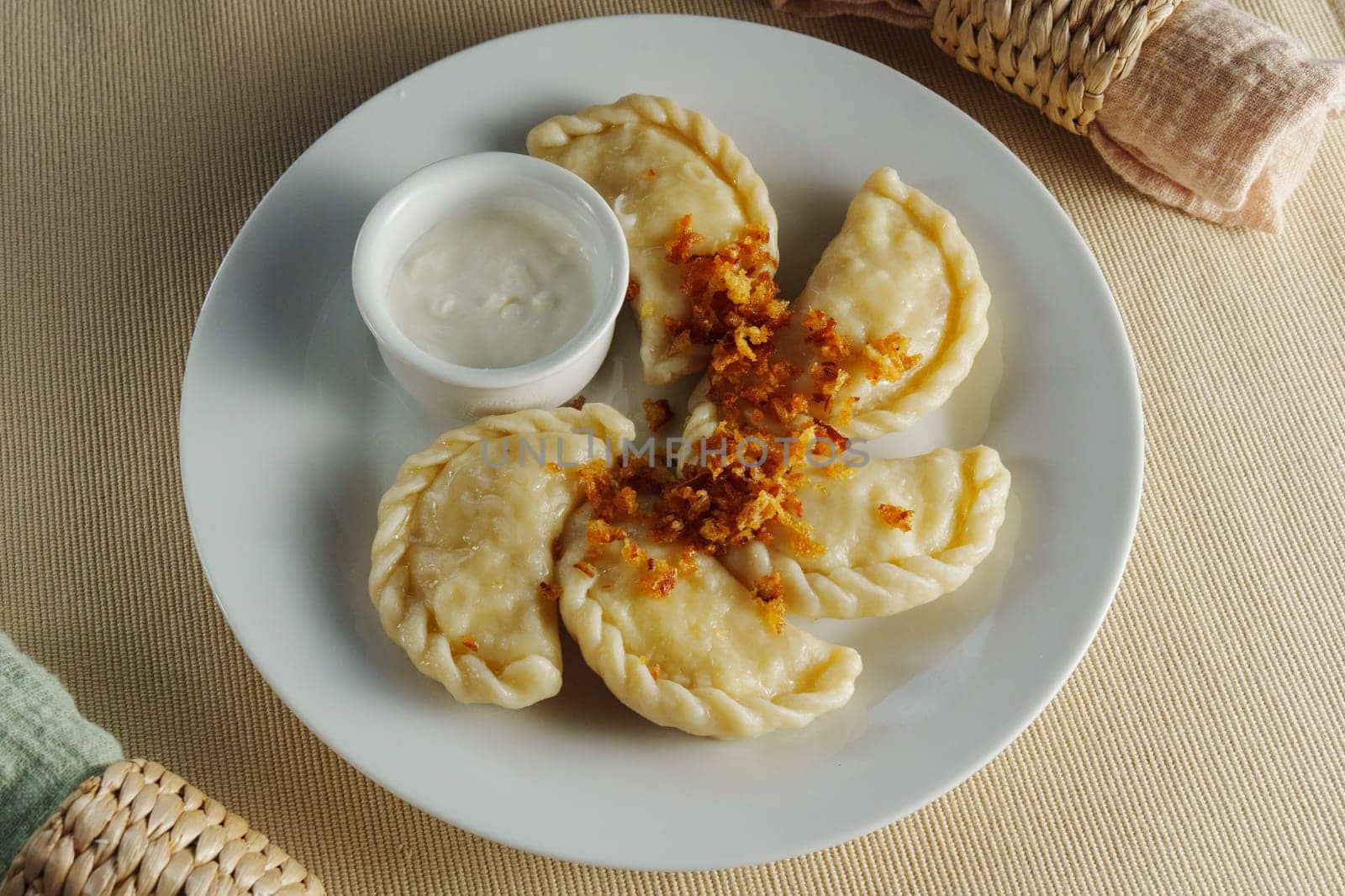 A plate of homemade dumplings showcases their delicate textures, topped with crispy bits and accompanied by a creamy dip, inviting for a cozy meal.