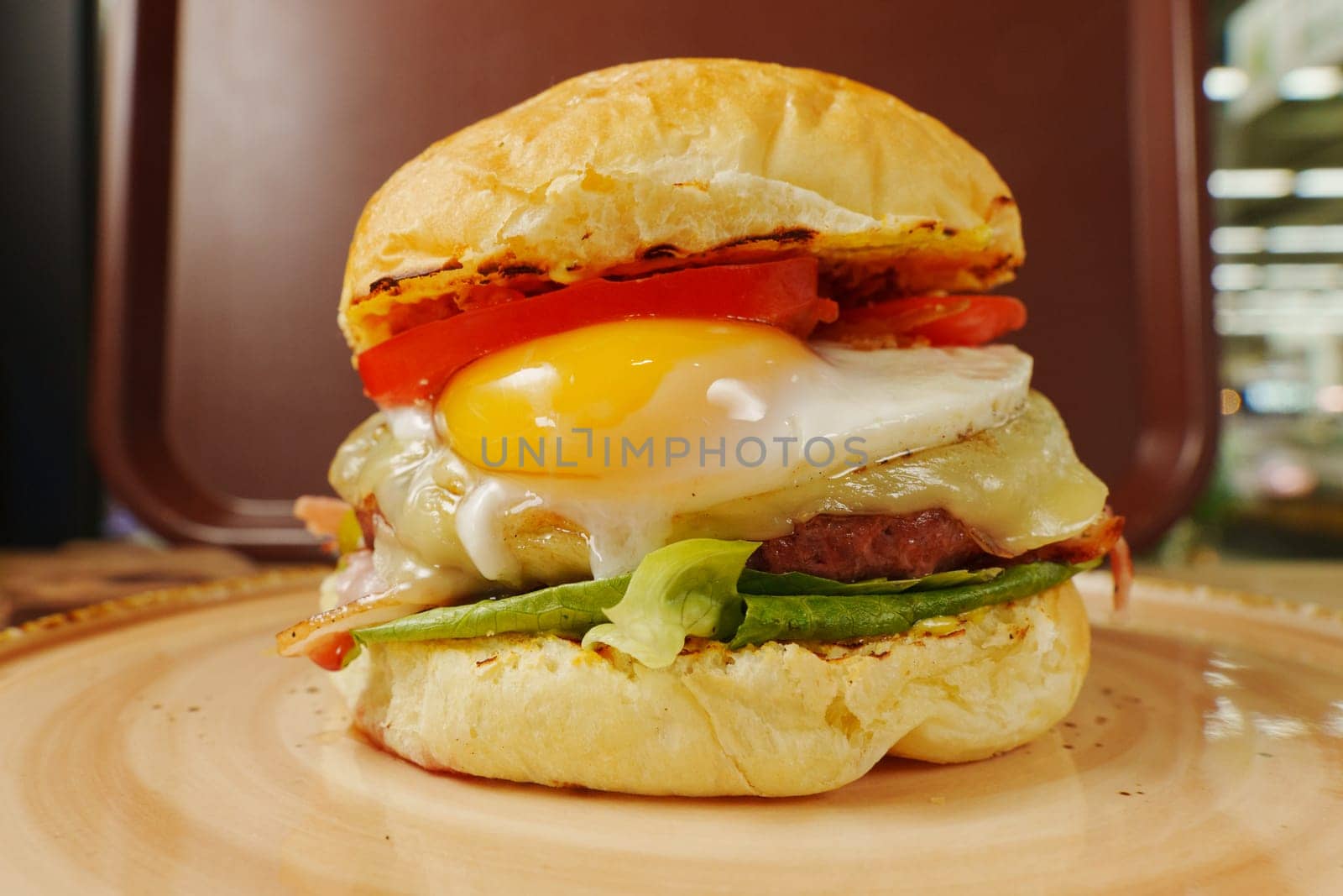 Breakfast burger features a perfectly fried egg, fresh tomatoes, and crispy lettuce layered with savory bacon and cheese