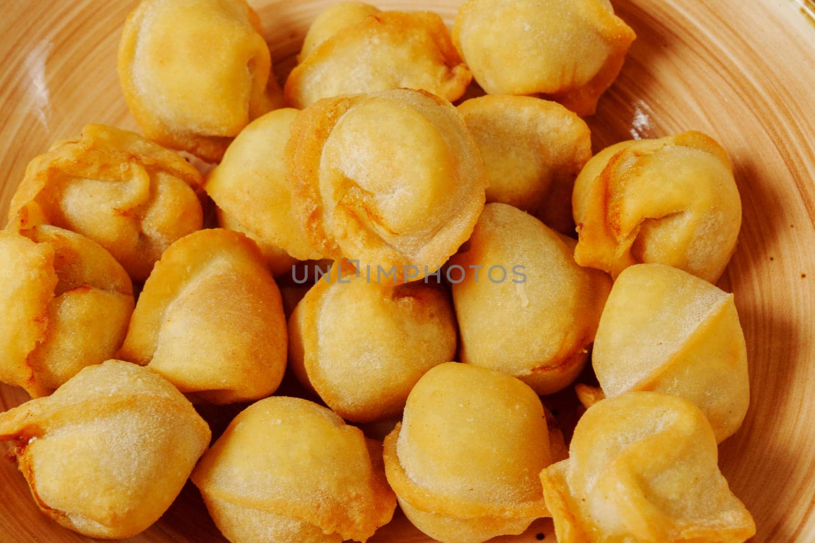 A delightful collection of golden-brown dumplings fills a cozy wooden bowl, their crispy edges promising a savory treat.