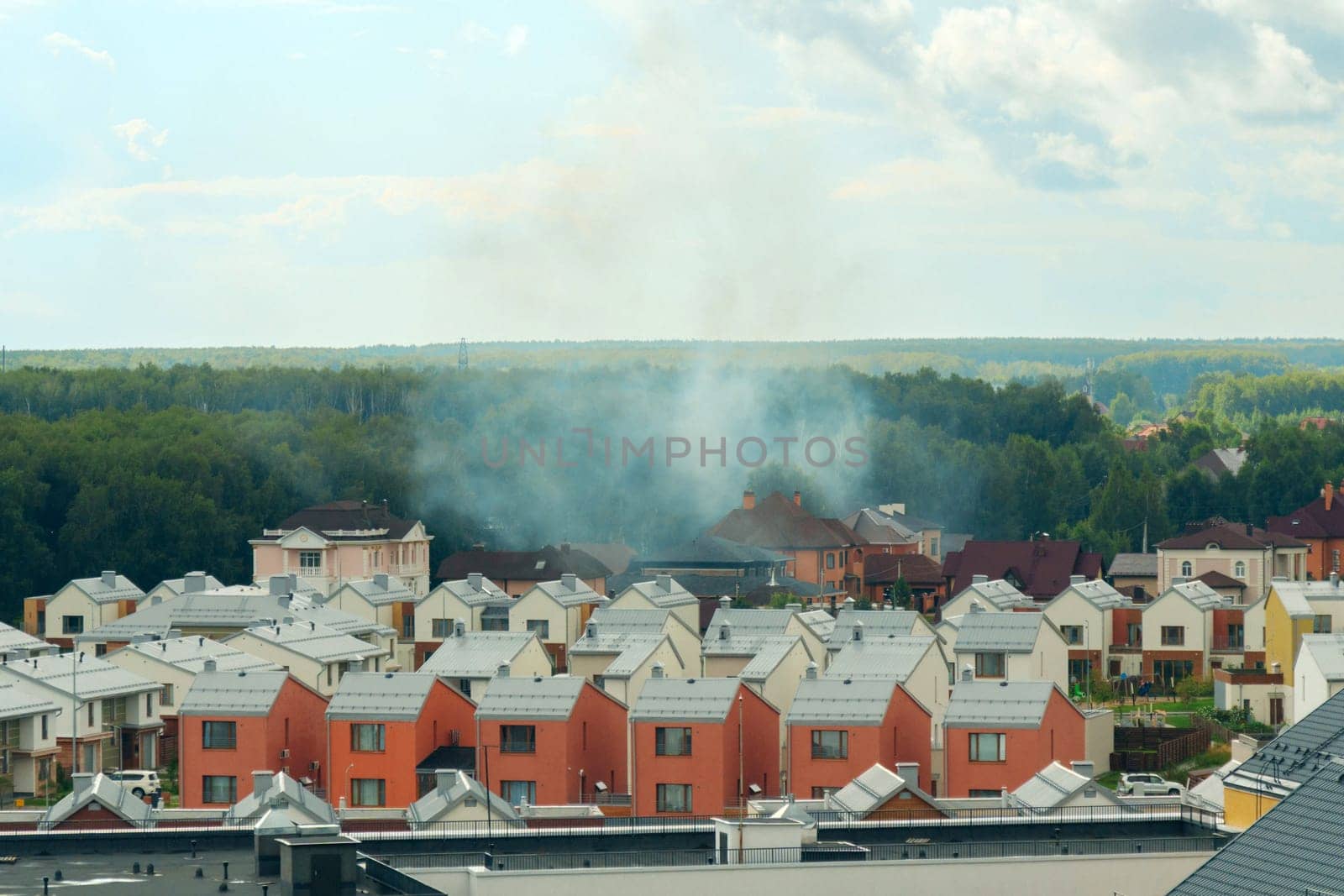 Smoke rises from a residential area near a forest during the afternoon hours in a suburban neighborhood