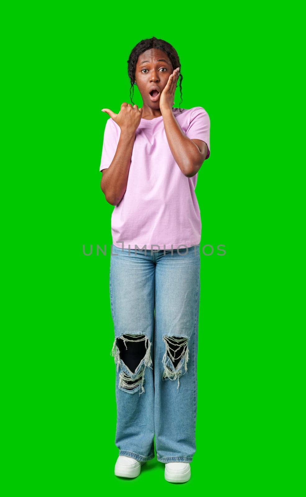 A young girl stands confidently pointing to the right against a bright green backdrop in studio