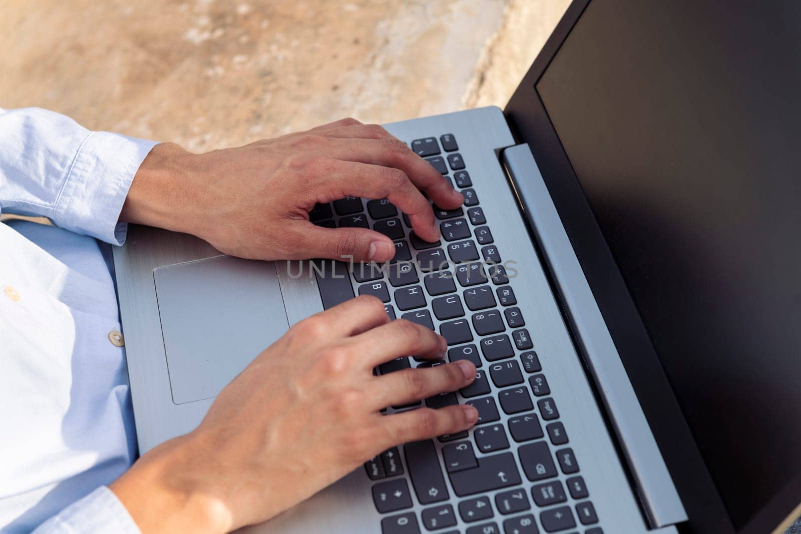 from above cropped unrecognizable female entrepreneur hands typing on laptop while sitting on stone bench in park and working remotely