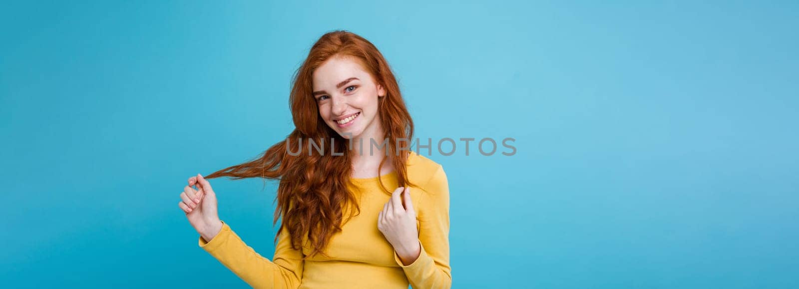 Portrait of happy ginger red hair girl with freckles smiling looking at camera. Pastel blue background. Copy Space.