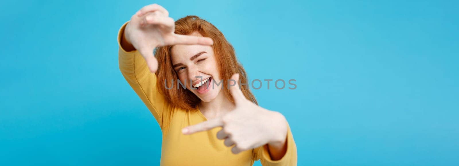 Portrait of young beautiful ginger woman with freckles cheerfuly smiling making a camera frame with fingers. Isolated on white background. Copy space