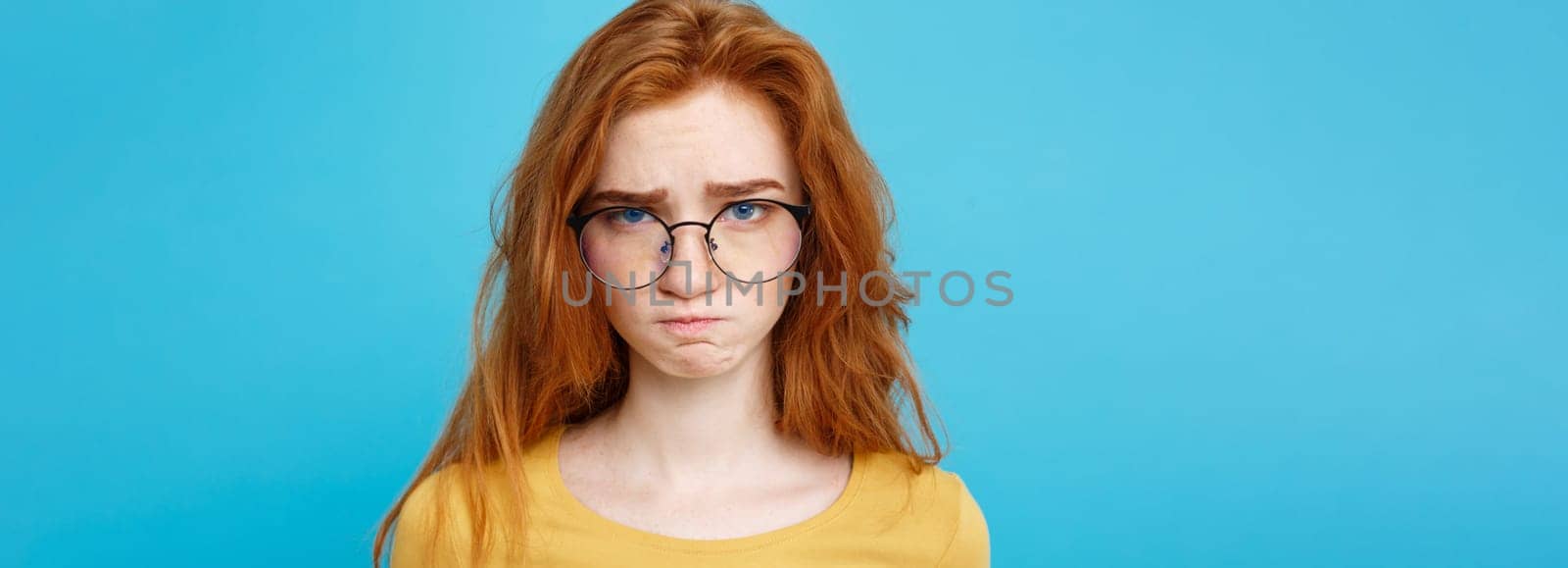 Headshot Portrait of happy ginger red hair girl with freckles smiling looking at camera. Pastel blue background. Copy Space