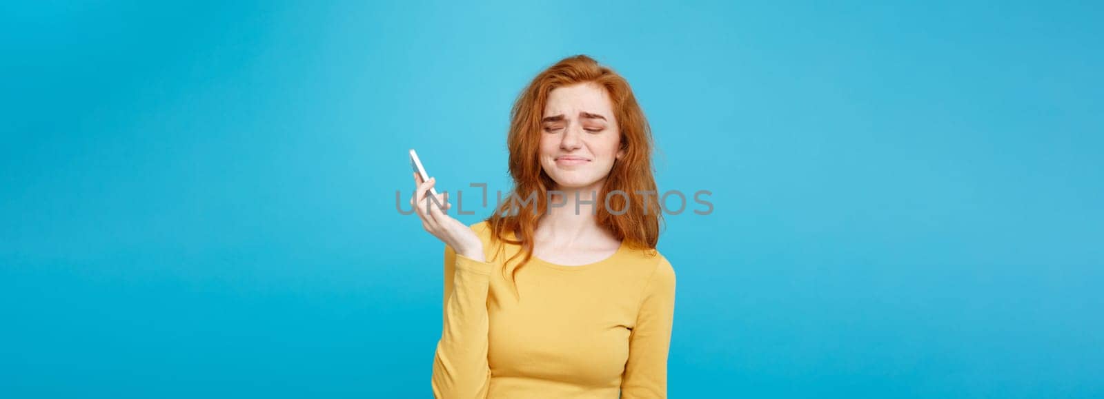 Lifestyle concept - Portrait of a shocked surprised girl in yellow dress talking on mobile phone. Isolated on Blue Pastel Background. Copy space.