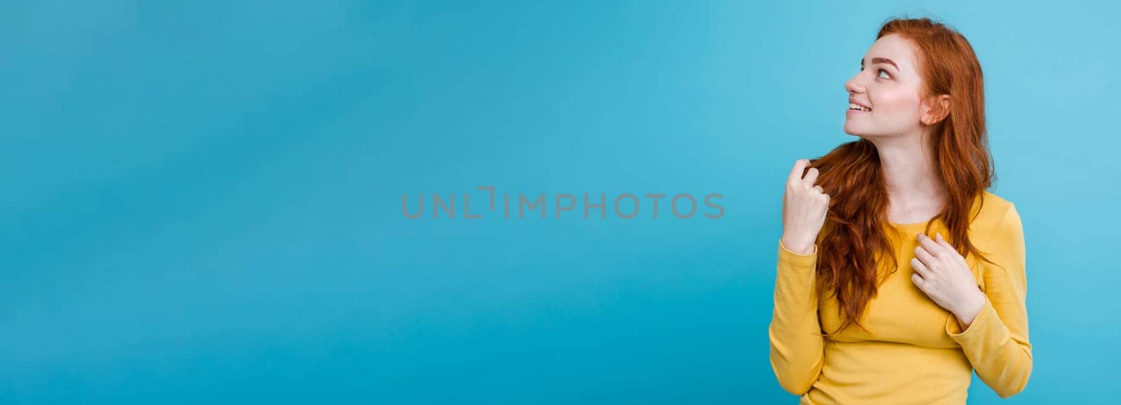 Portrait of happy ginger red hair girl with freckles smiling looking at camera. Pastel blue background. Copy Space.