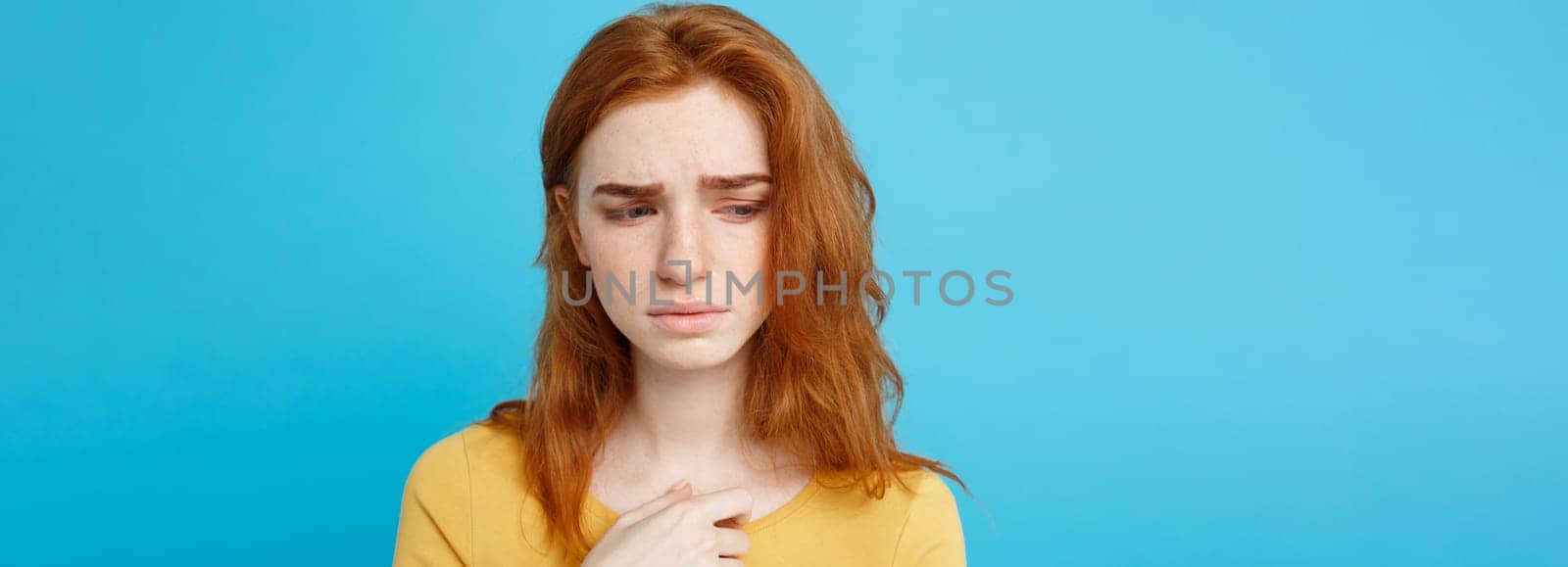 Headshot Portrait of tender redhead teenage girl with serious expression looking at camera. Caucasian woman model with ginger hair posing indoors.Pastel blue background. Copy Space