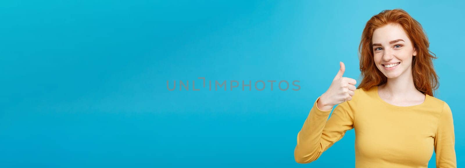 Portrait of young stylish freckled girl laughing with showing thumps up at camera. Copy space