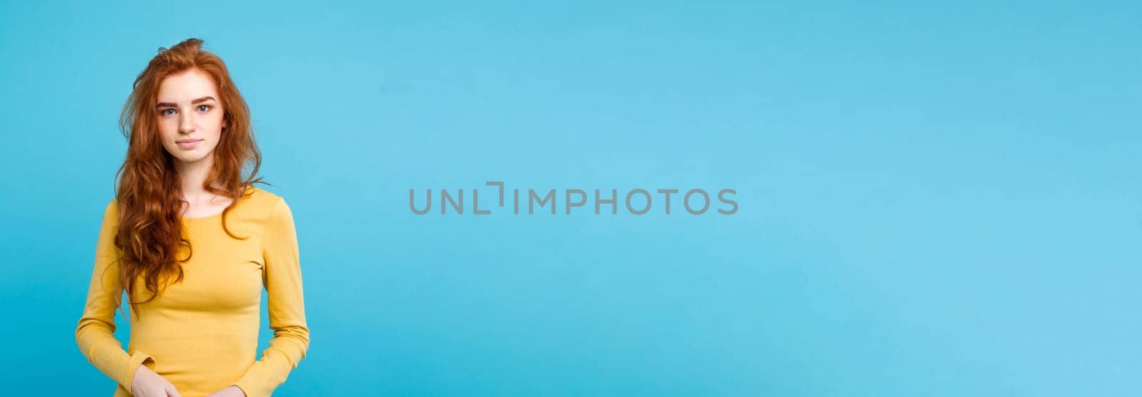 Portrait of young beautiful ginger woman with tender serious face crossing arms looking at camera. Isolated on pastel blue background. Copy space.