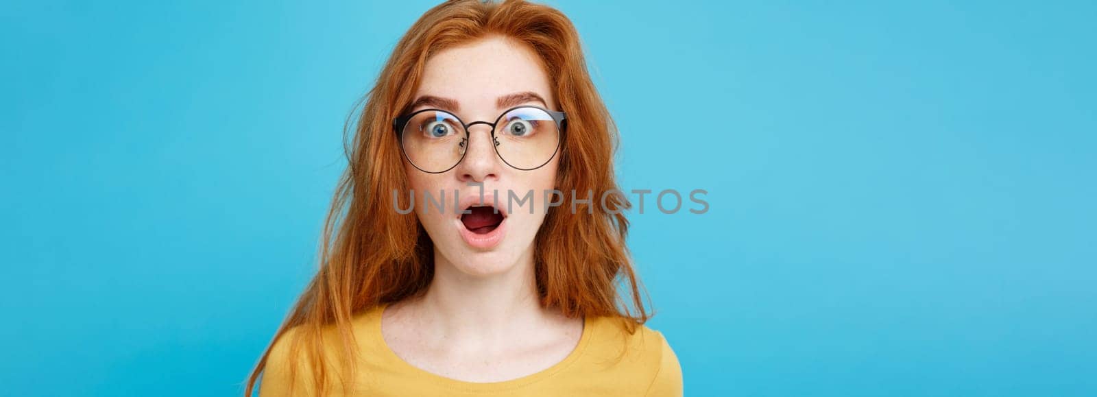 Close up Portrait young beautiful attractive redhair girl with eyeglass shocking with something. Blue Pastel Background. Copy space