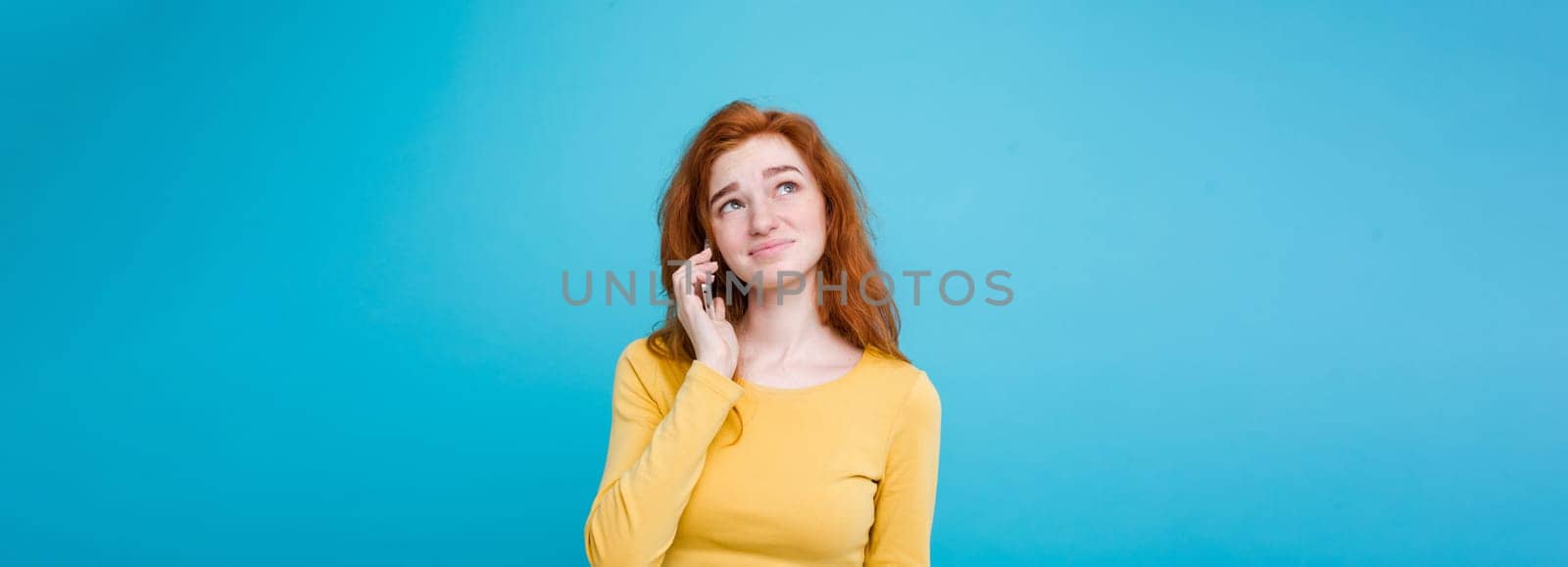 Lifestyle concept - Portrait of ginger red hair girl with shocking and stressful expression while talking with friend by mobile phone. Isolated on Blue Pastel Background. Copy space.