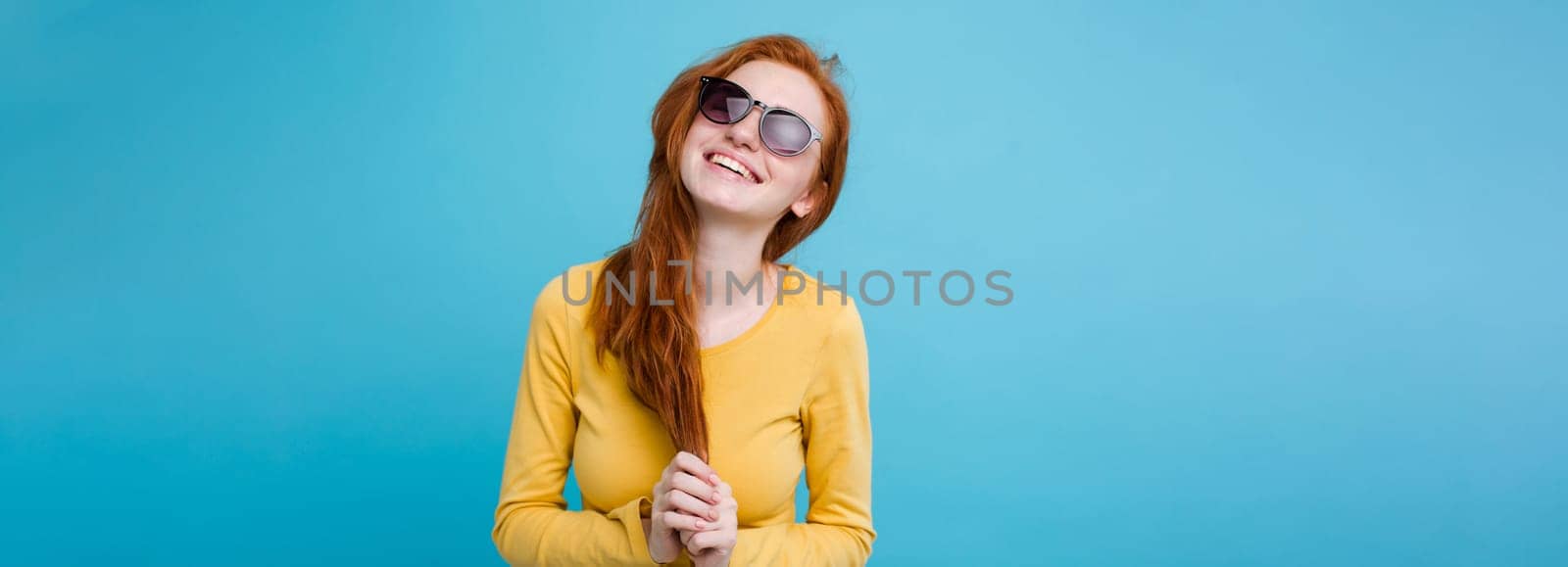 Portrait of happy ginger red hair girl with freckles smiling looking at camera. Pastel blue background. Copy Space.