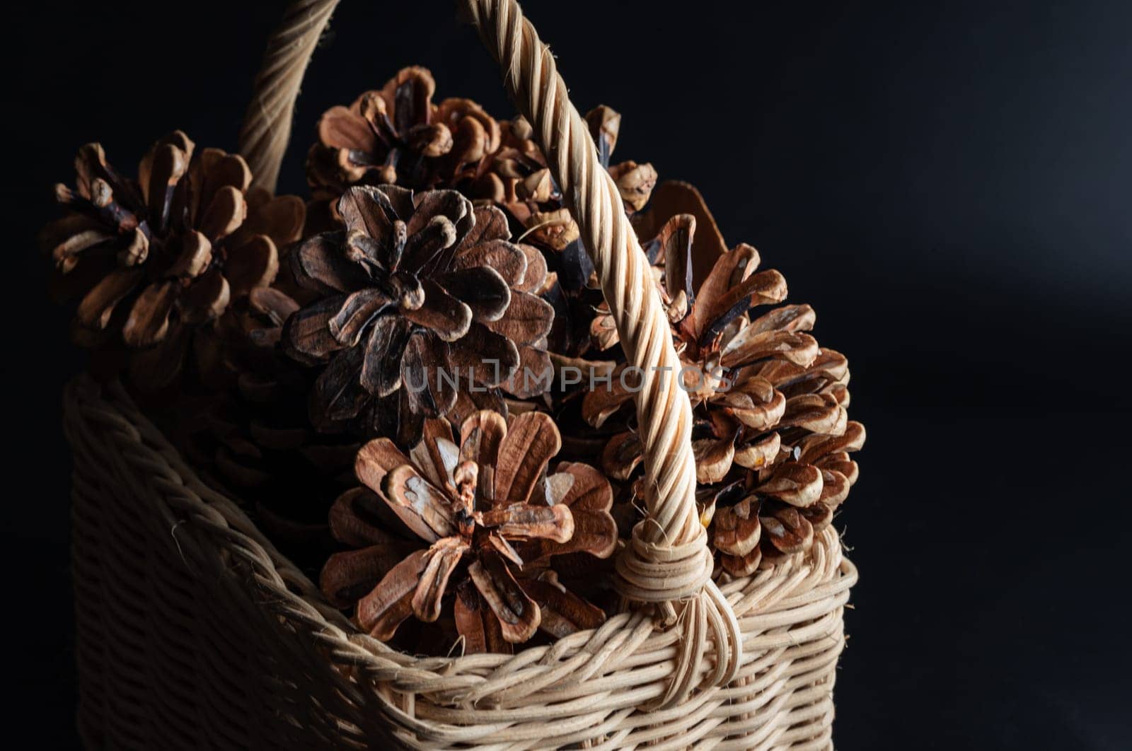Pine cones in Wicker basket on dark background. Pine cones nice and dry and some are open up, Light and Shadow, use it as your Wallpaper, Poster and Space for text, Selective focus.