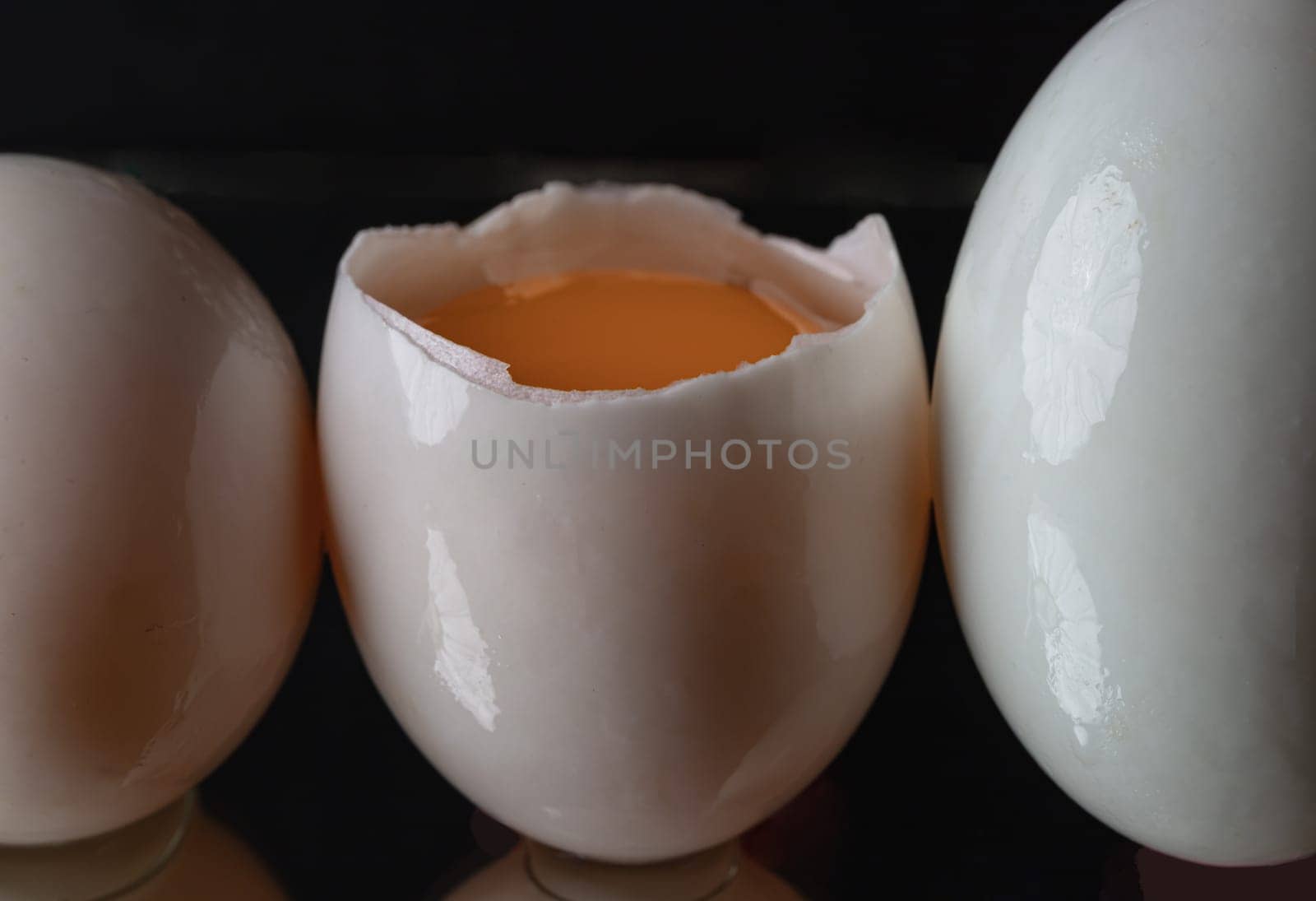 Three raw duck eggs are sitting in a row with an egg in the middle broken in half showing the yolk and white egg on dark background. use it as your Wallpaper, Poster and Space for text, Selective focus.
