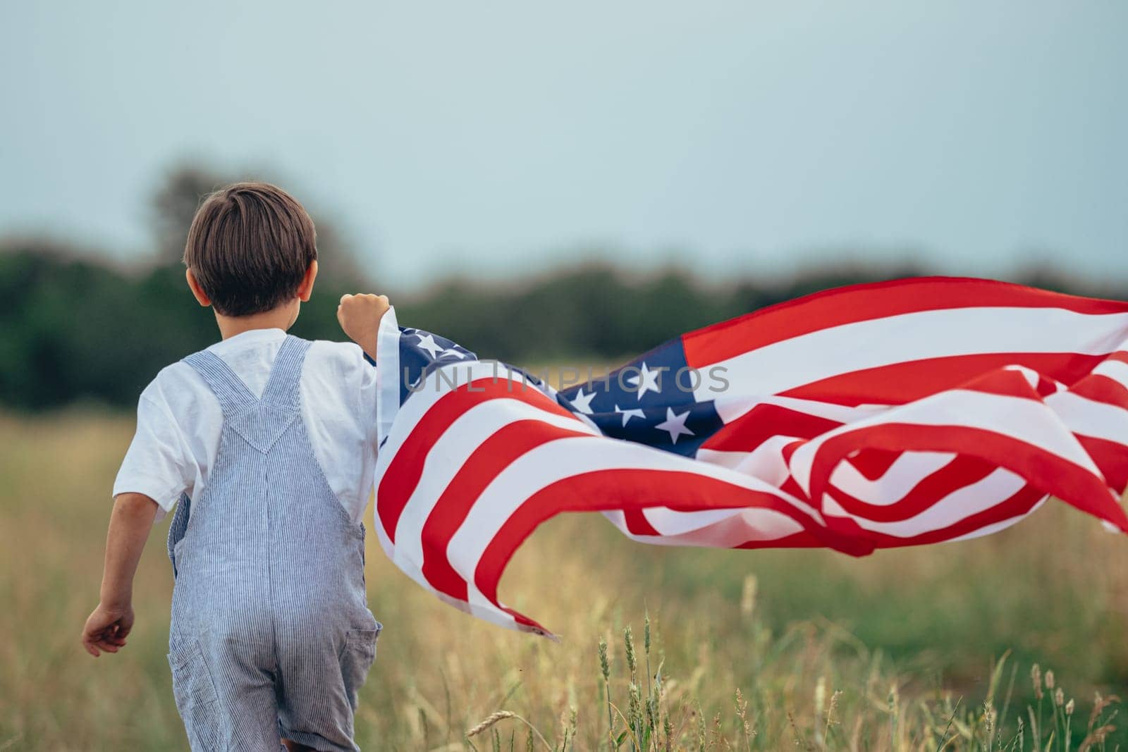 Cute boy - American patriot kid running with flag on rural countryside road Summer.USA, 4th of July - Independence day, celebration. US banner, memorial Veterans, election, America, labor