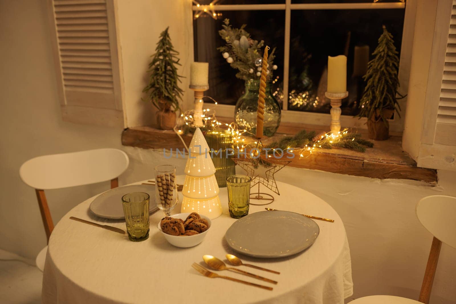 Cozy Christmas setting with a round table near the window, The table is decorated with a decorative Christmas tree in the center, Soft lighting from candles and garlands