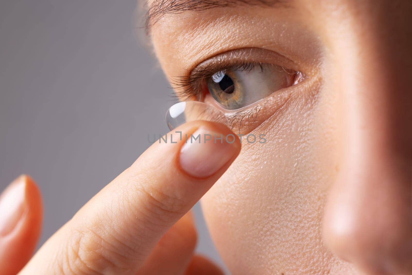 Young woman puts contact lens in her eye over white background. Eyewear, eyesight and vision, eye care and health, ophthalmology and optometry concept. Selective focus, close up