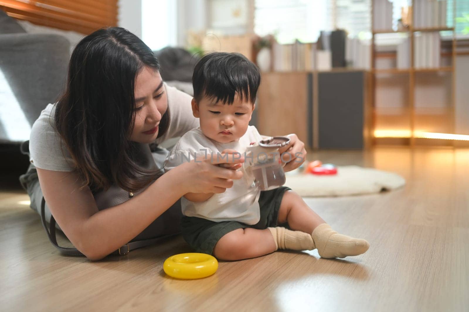 Young mother and her baby sitting on wooden floor in a cozy living room. Child care, parenting and family concept.