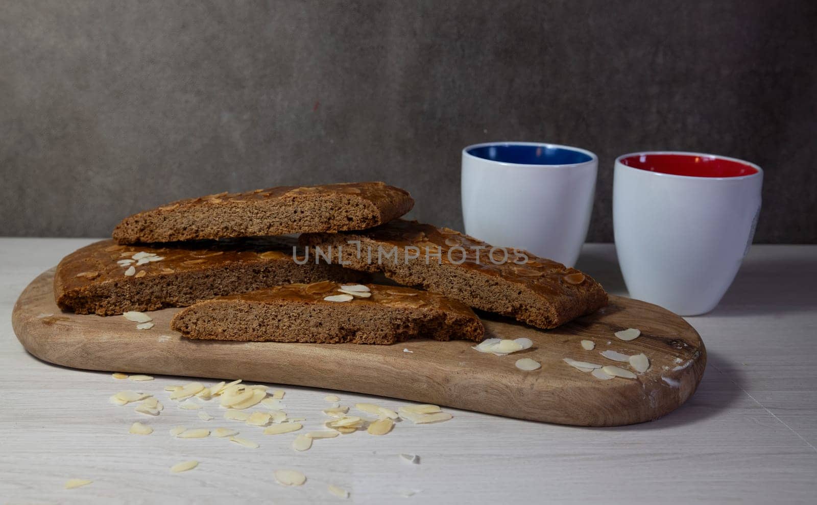 homemade speculaas cake, dSliced homemade almond biscotti displayed on a wooden board, accompanied by two colorful coffee mugs, creating a cozy and inviting atmosphere ideal for coffee breaks.