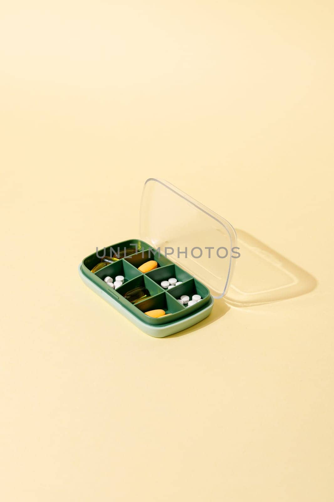 Green plastic pill box with various pills and vitamins for every day, copy space.