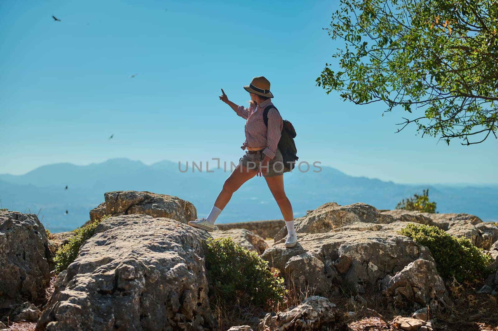 A woman in casual hiking attire explores a rocky mountain terrain, surrounded by breathtaking landscapes. Her adventurous spirit is evident as she immerses herself in nature's beauty.