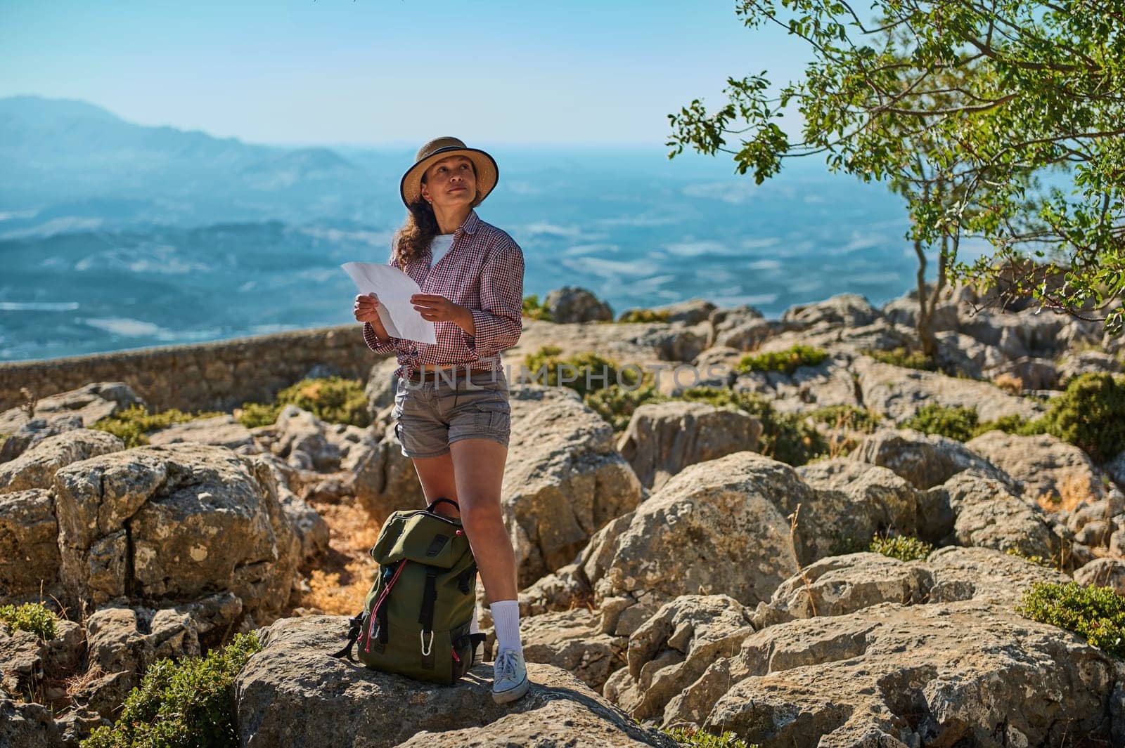 A woman in casual outdoor attire navigates a rocky terrain with a map. The image captures a sense of adventure and exploration, set against a breathtaking natural backdrop.