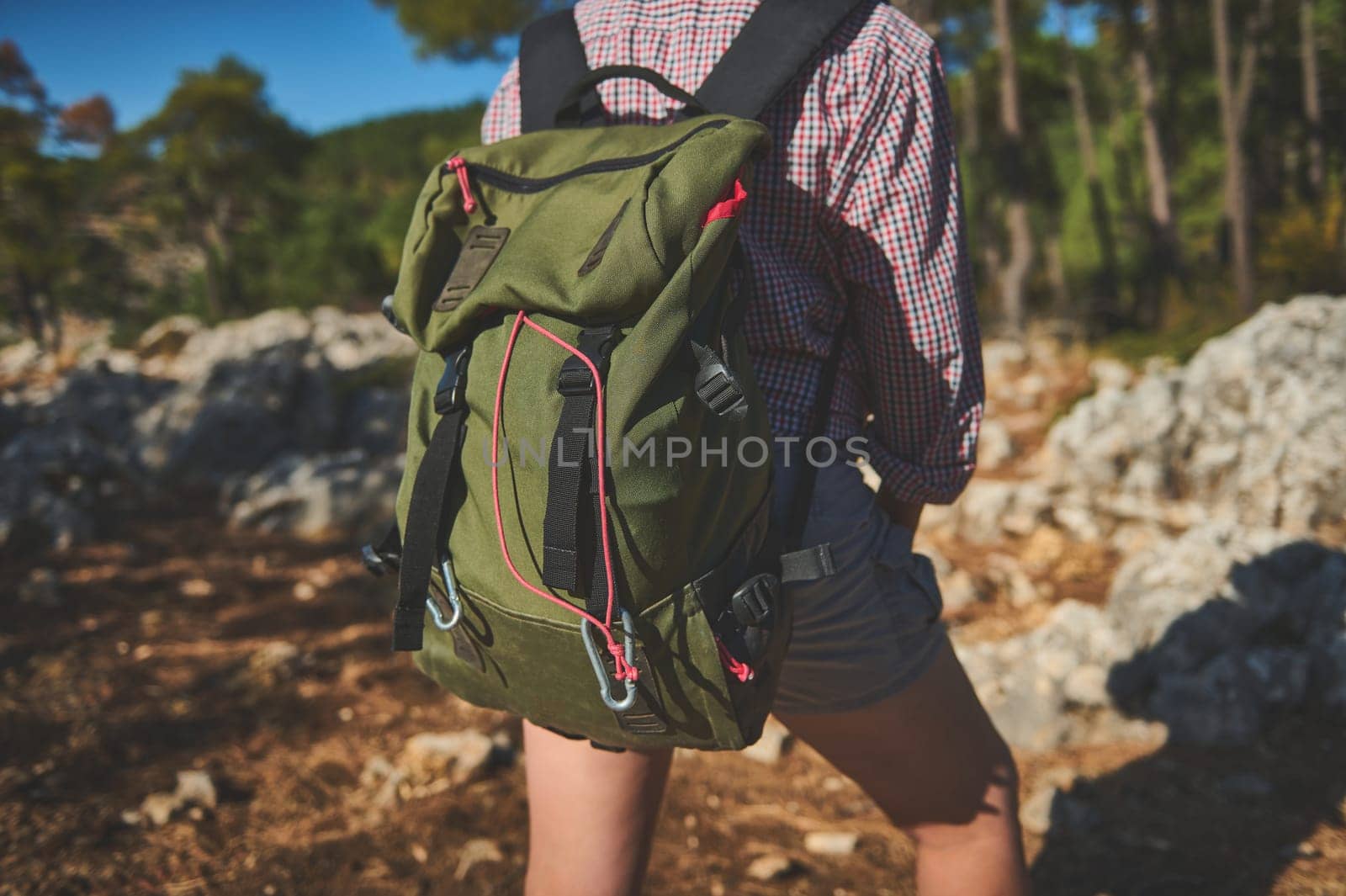 A person wearing a green backpack while hiking through a scenic forest trail. Outdoors, nature, adventure.