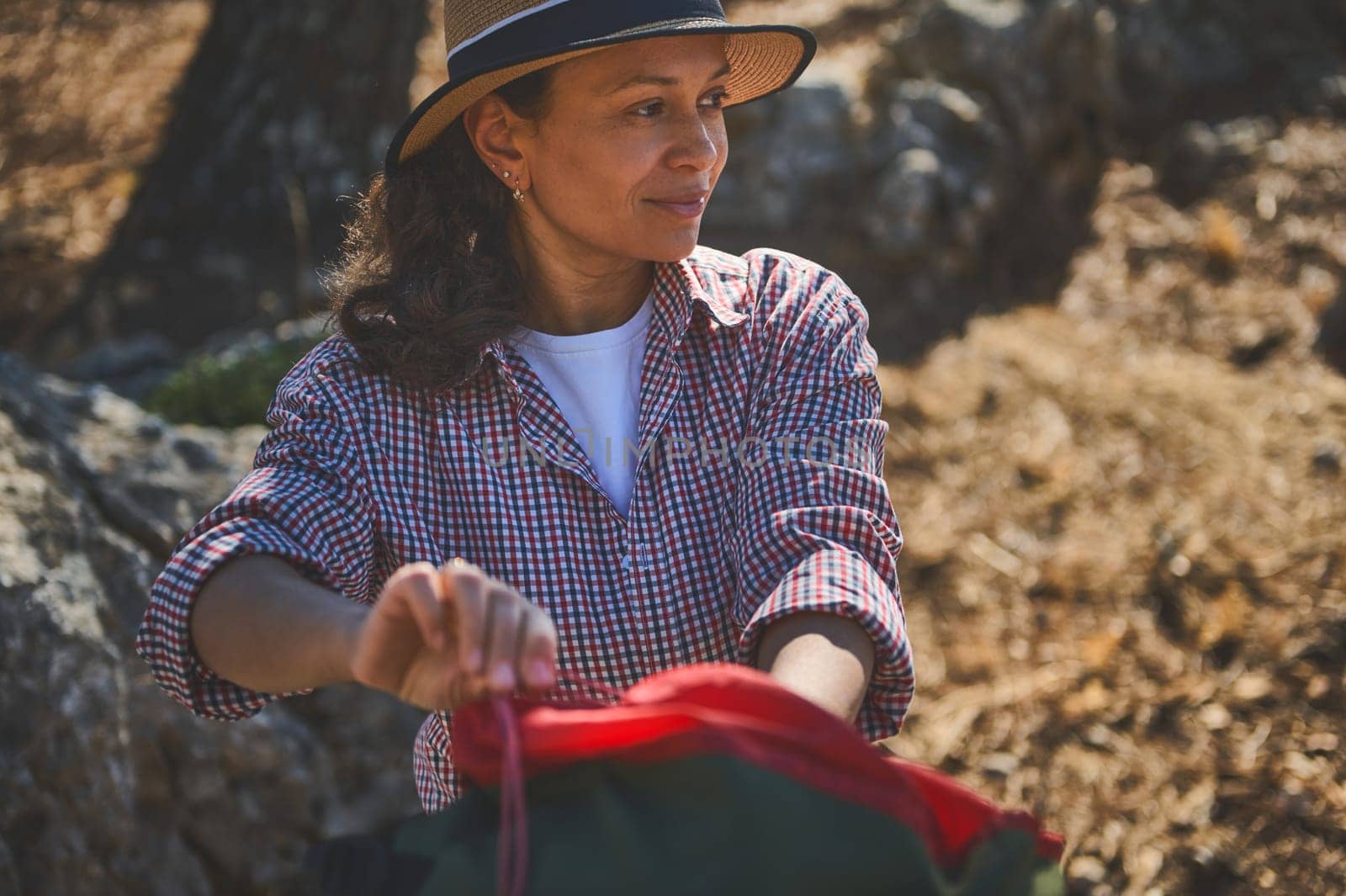A woman in a plaid shirt enjoying a moment of tranquility during a hike in a sunny, serene natural setting.