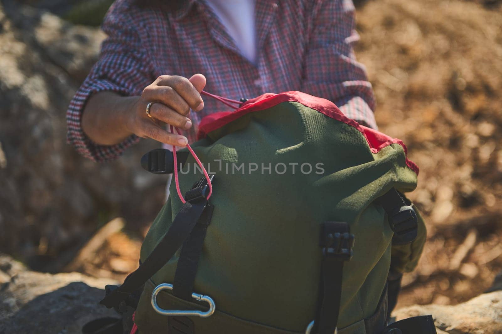 A close-up view of a person adjusting the straps of a green backpack, highlighting outdoor exploration and adventure. The focus is on the hands and the backpack in a natural setting.