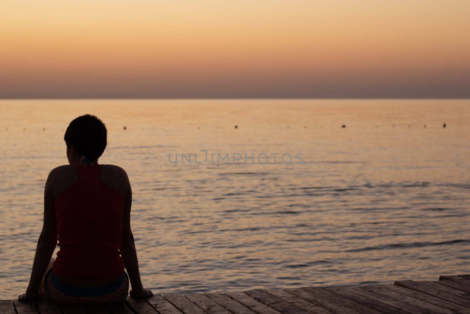 A person sitting on a pier looking at the sea during a beautiful sunrise over the horizon