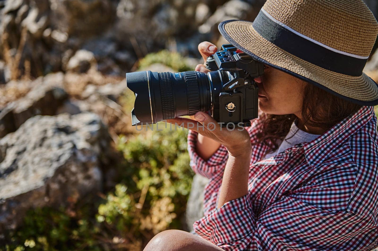 A woman in casual attire and a straw hat takes photographs in an outdoor natural setting. Captures the essence of outdoor photography and creativity.