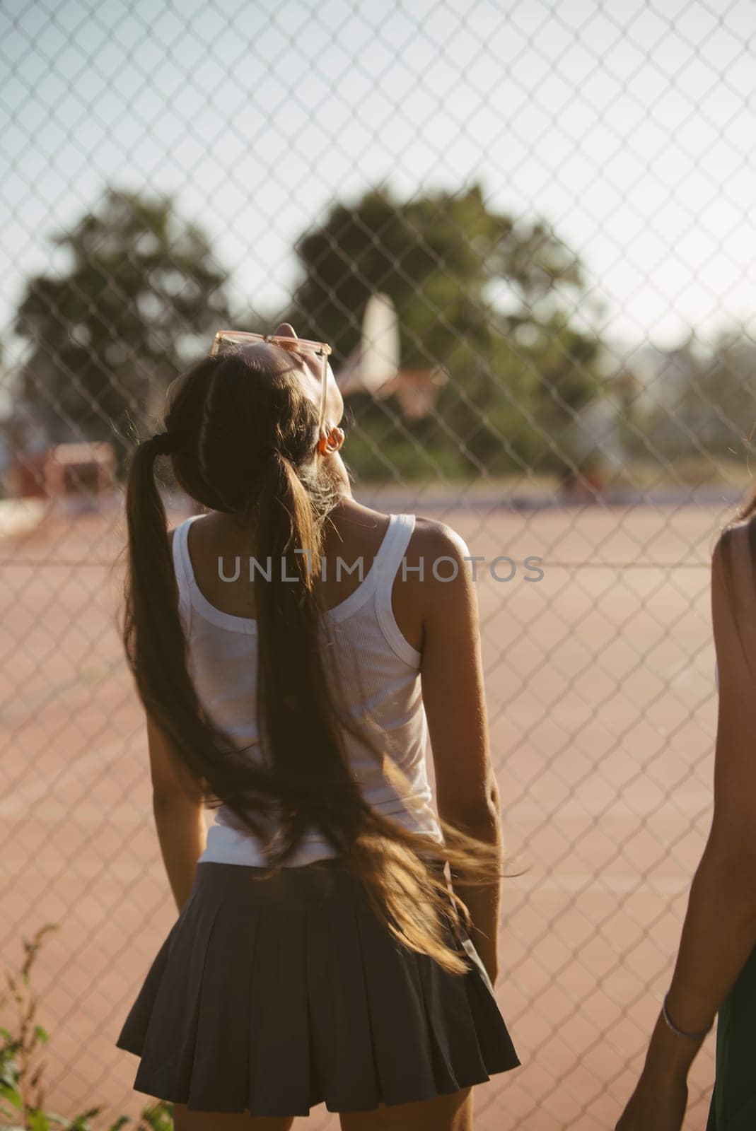 Two teenagers relax happily by a basketball court, enjoying sunlight and sharing a joyful moment outdoors