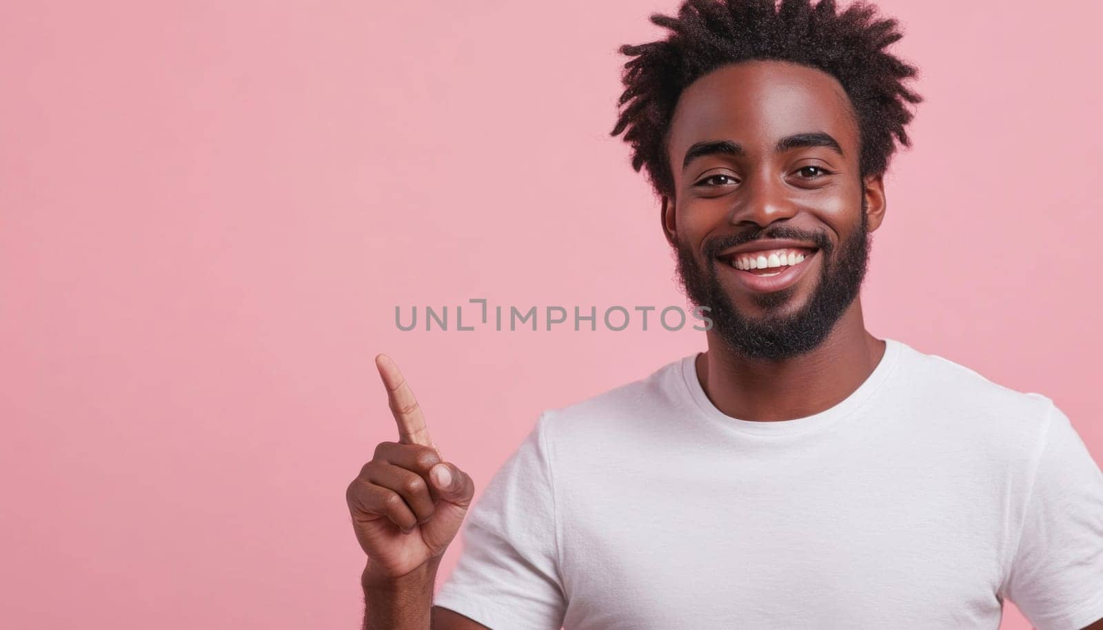 Young adult man is smiling and pointing up with his index finger against a pink background