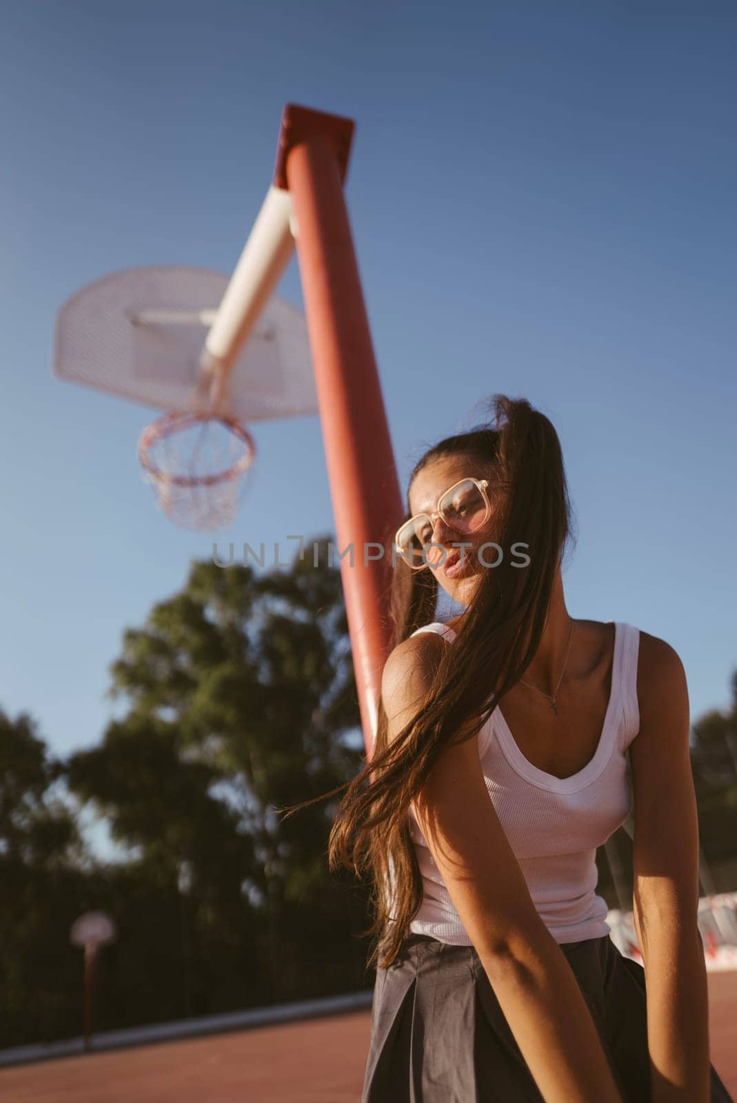 A vibrant young woman poses at a basketball court under the warm sun, showcasing her energetic style.