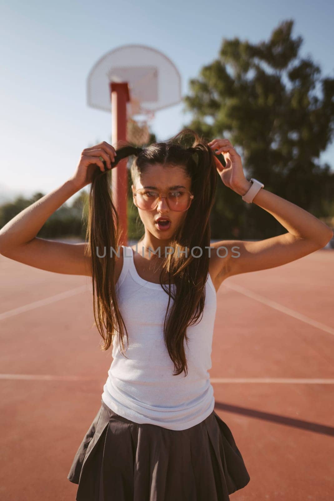 A cheerful girl is having fun enjoying a sunny day on the basketball court, showcasing her playful hairstyles