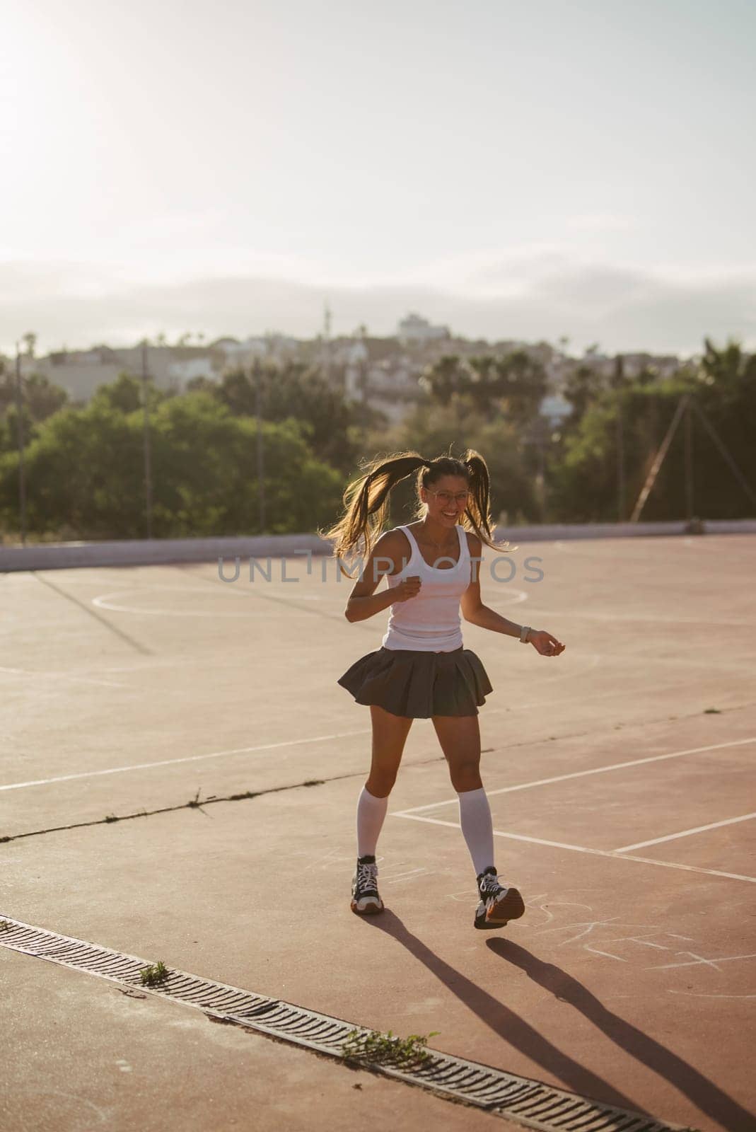A lively and cheerful girl joyfully enjoys running on a sunlit sports court, embodying pure energy and freedom
