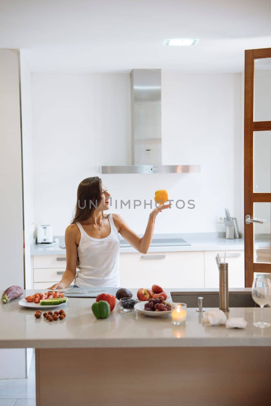 A woman showcases colorful fruits in her modern kitchen, promoting a healthy lifestyle and wellbeing