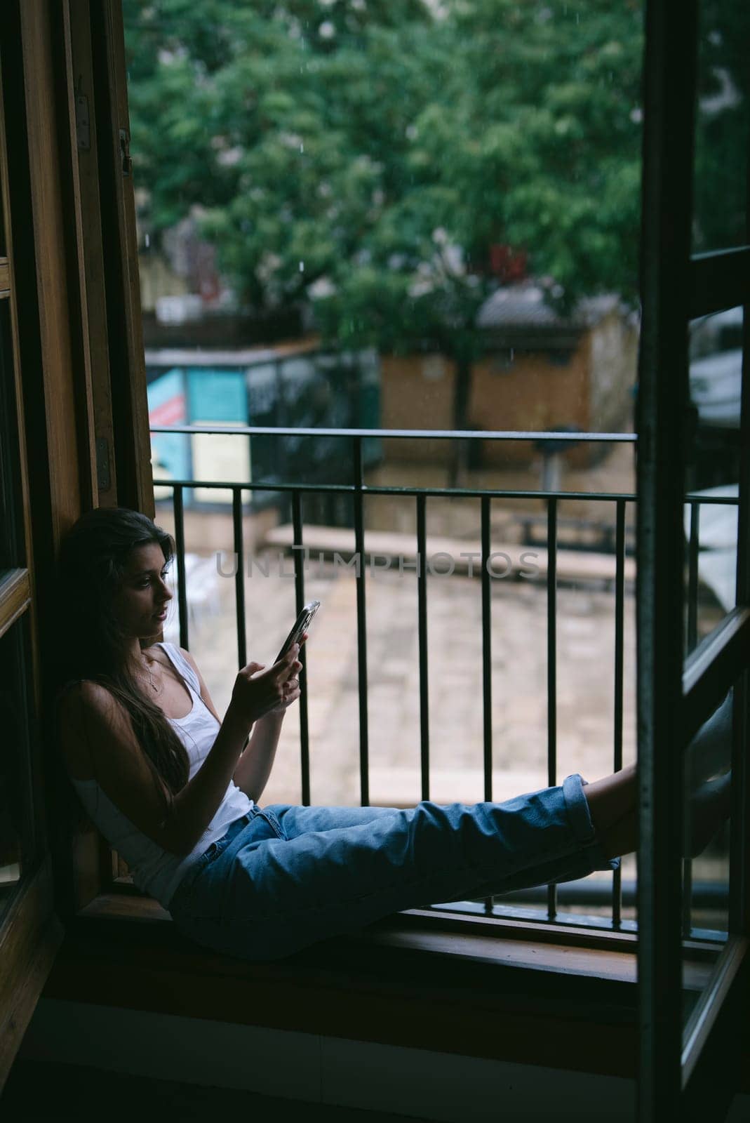 A serene scene depicts a person savoring a tranquil moment while lounging on a cozy balcony using their phone
