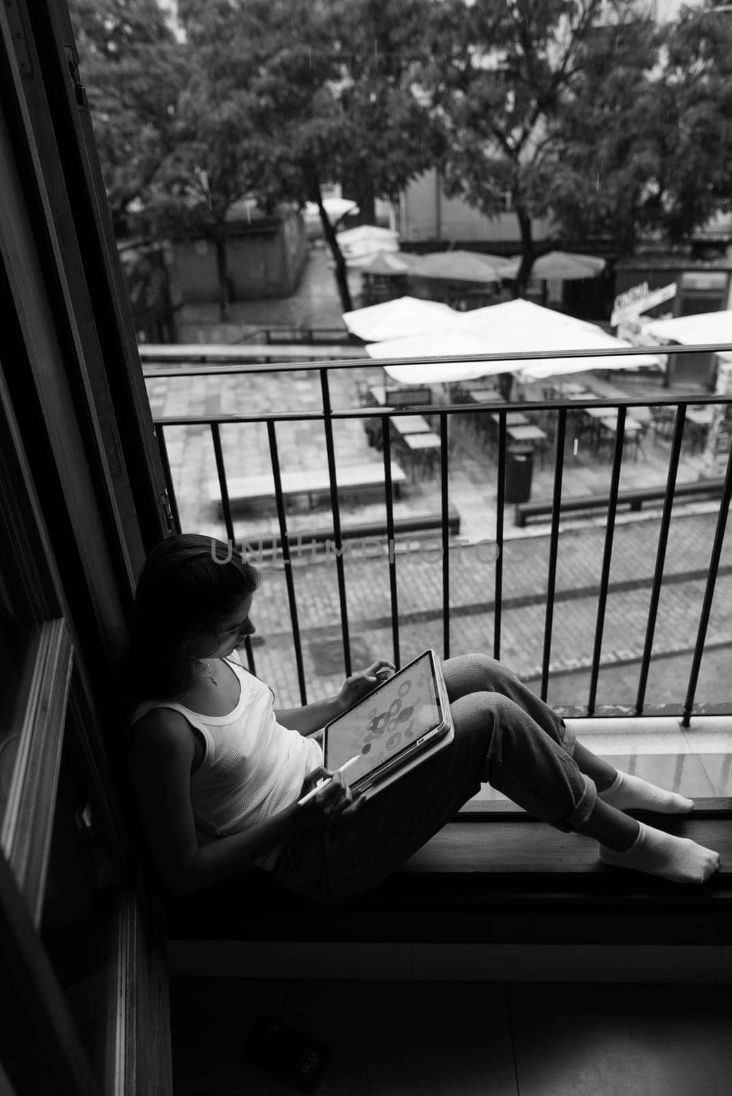 A tranquil black and white photograph showcasing a young woman deeply engrossed in a captivating book by the window