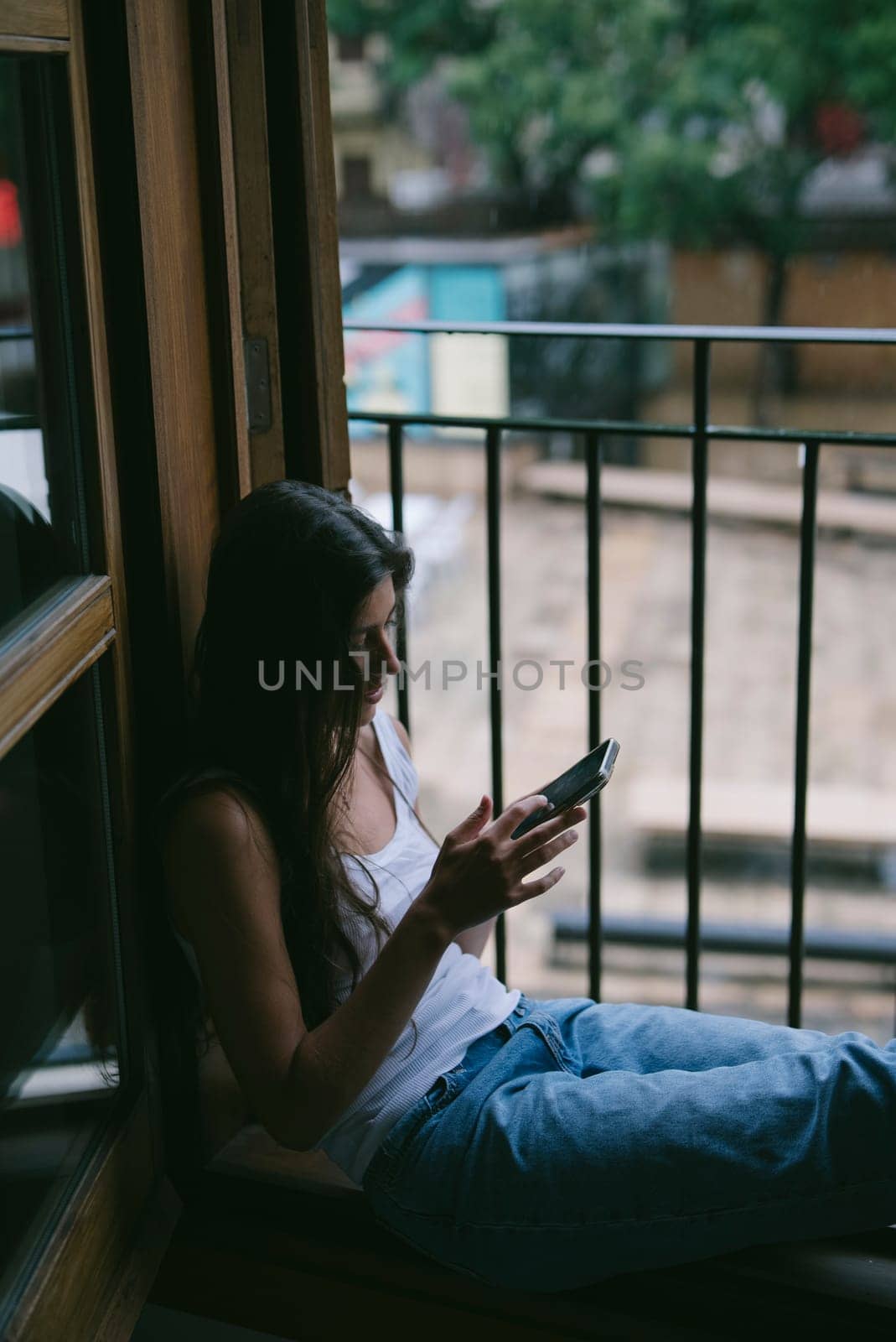 A tranquil and serene moment was beautifully captured showing a woman completely engrossed in her phone by a window