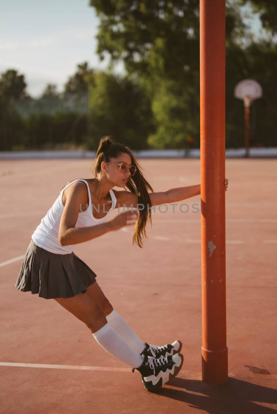 A dynamic and energetic young woman dressed in sporty attire joyfully skates playfully near a basketball pole